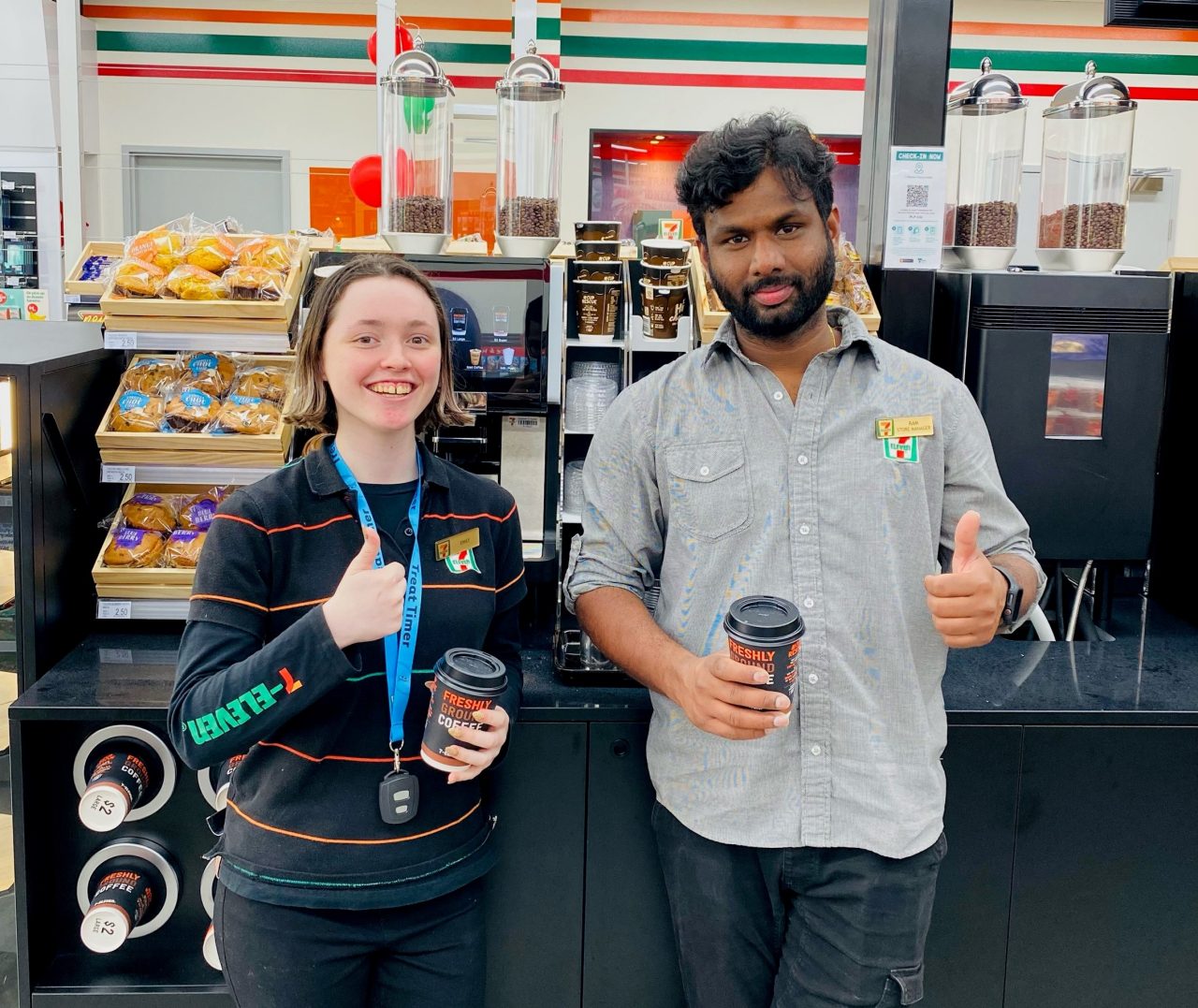 Emily and Ram from 7-Eleven Delacombe in their uniforms, smiling, in front of coffee machine.