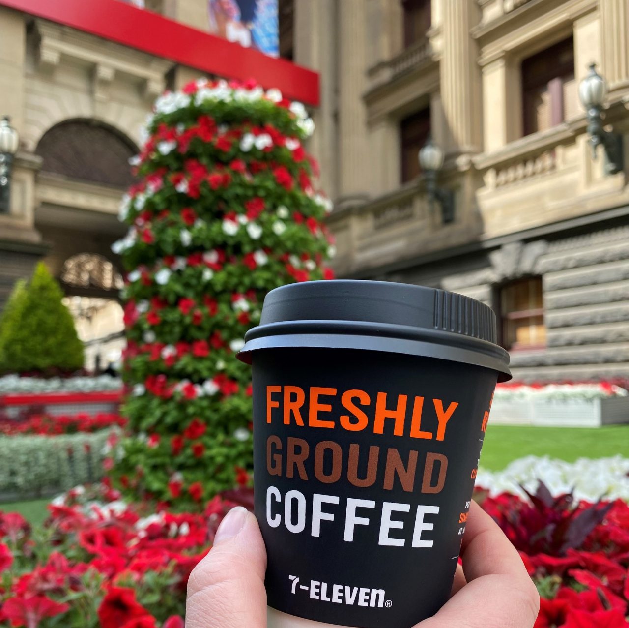 A cup of 7-Eleven coffee with Christmas displays of flowers in the background
