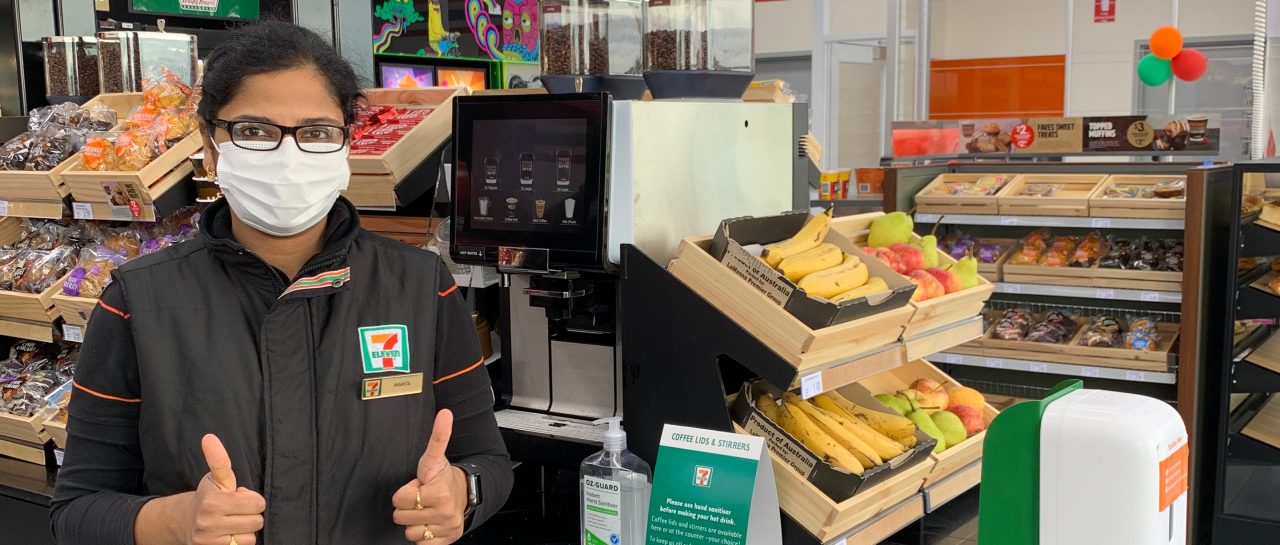 Image of female 7-Eleven team member in store. She is wearing a mask and has her thumbs up.