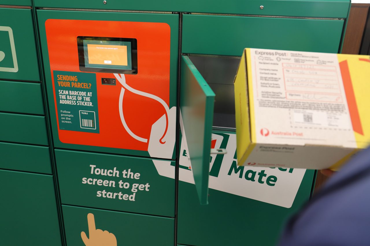 A 7-Eleven ParcelMate Locker with a hand holding an Australia Post parcel in front of it.