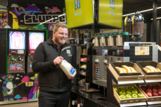 A 7-Eleven team member in-store with milk and fresh produce.