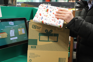 Hands packing wrapped Christmas present into a 7-ELeven ParcelMate postage box.