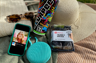 A picture of a picnic blanket with a summer hat, sunglasses, a Slurpee Cup, a pack of 7-Eleven sushi, a portable music speaker and an iphone playing music. Artist Jack River's single is pictured in the screen.