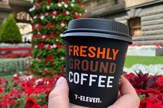 A cup of 7-Eleven coffee with Christmas displays of flowers in the background