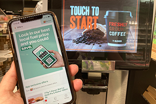 Picture of a phone with My 7-Eleven App fuel price lock on the screen in front of a 7-Eleven Coffee Machine.