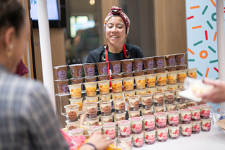 A picture of a 7-Eleven team member, she is smiling and standing behind a display of new products.