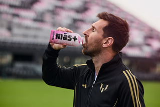 image of Messi on a football field drinking Más+ by Messi